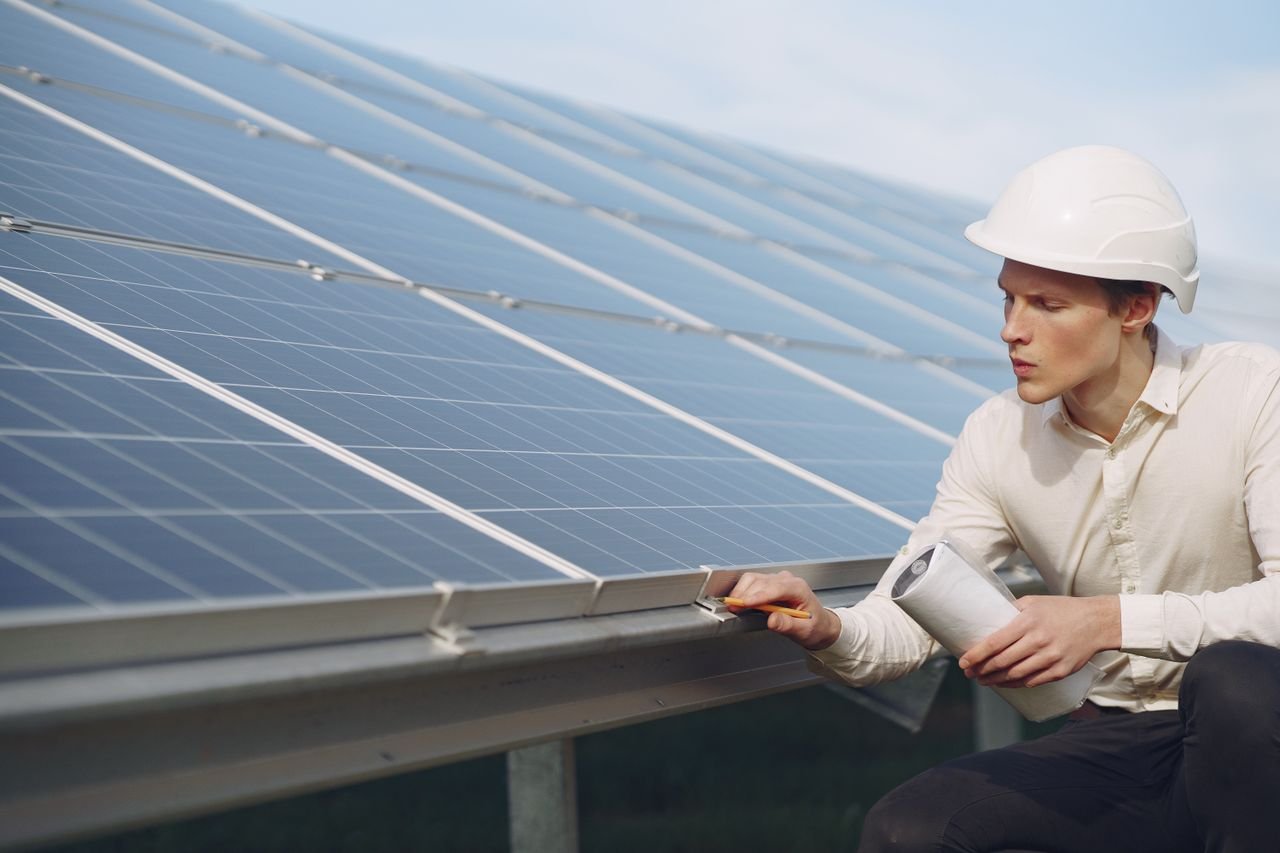 about-us Focused young male employer in formal wear and hardhat working on solar panel station and checking details of modules